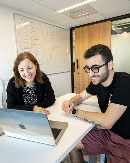 Alina Oprea (left) talks to a student while they both view a laptop