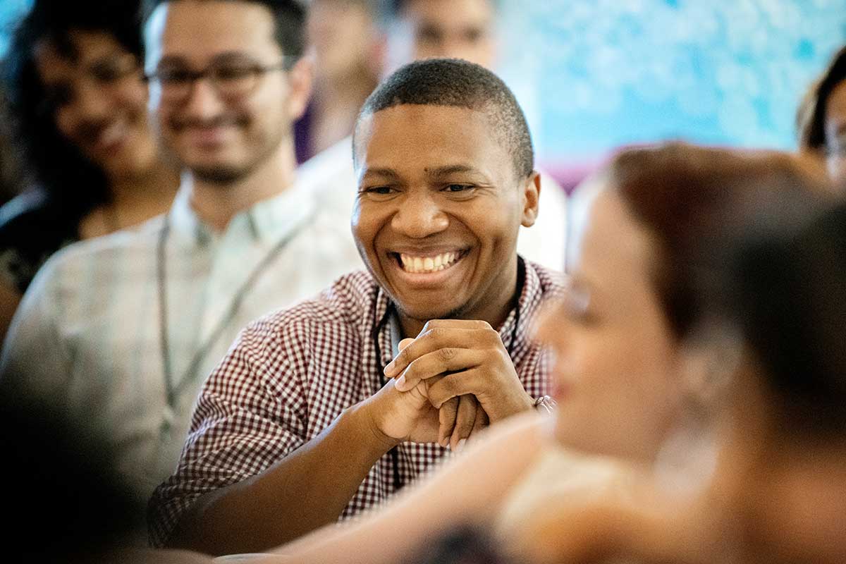 A student smiles in the middle of several other students while viewing a presentation