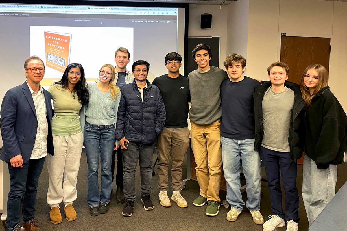 Ten members of Northeastern Blockchain post for a photo standing in front of a presentation screen
