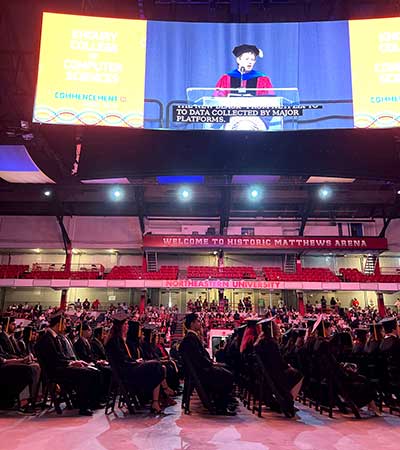 Khoury College graduates watch Dean Elizabeth Mynatt deliver a speech at the 2022 Khoury celebration