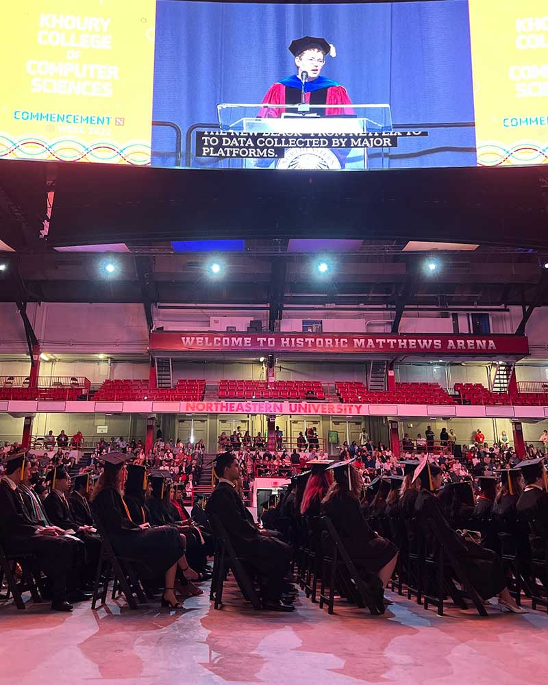 Khoury College graduates watch Dean Elizabeth Mynatt deliver a speech at the 2022 Khoury celebration