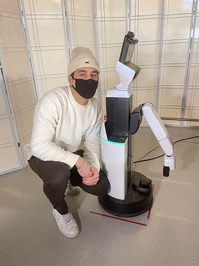 Stephen Alt kneels next to a robotic arm