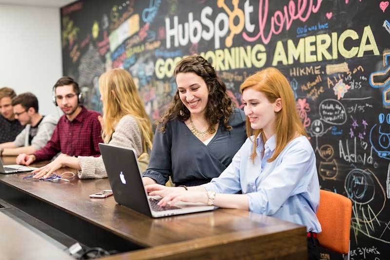 Two women work on a project together while looking at a laptop