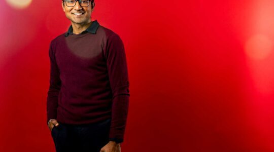 Vivek Kanpa smiles in front of a red background