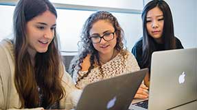 Three women work on a project in a Khoury classroom