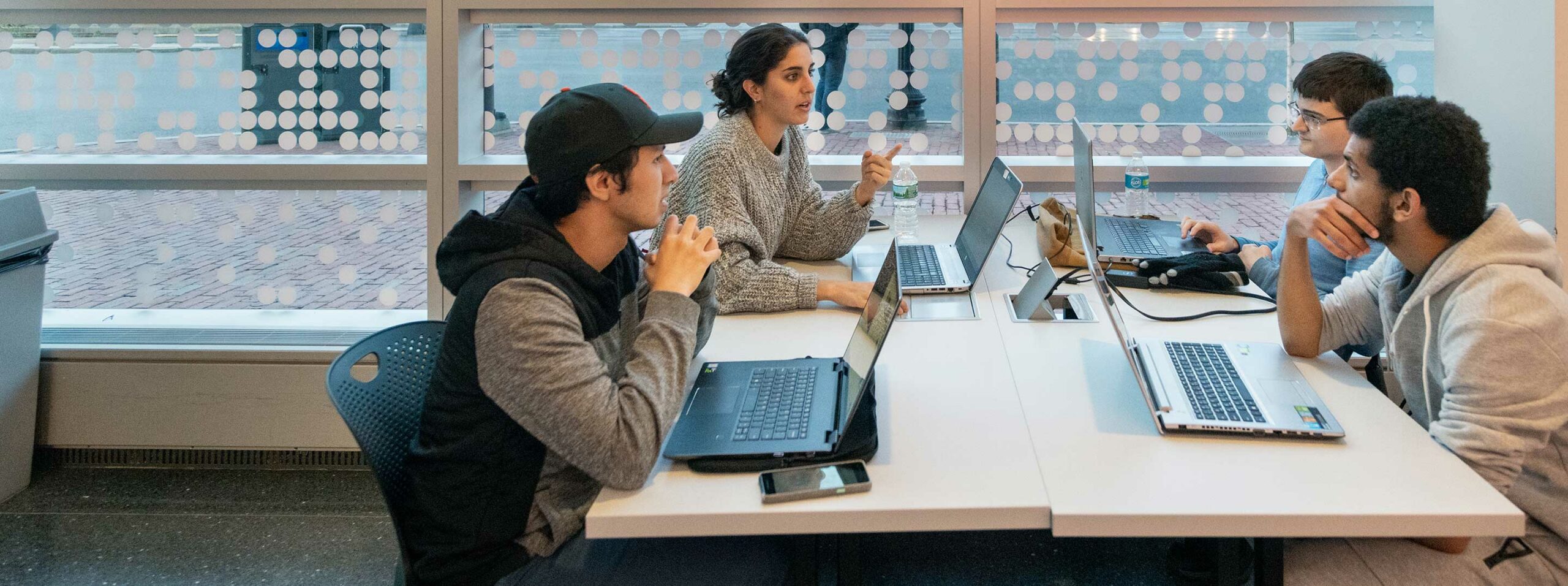 Four students discuss a project at a table in West Village H