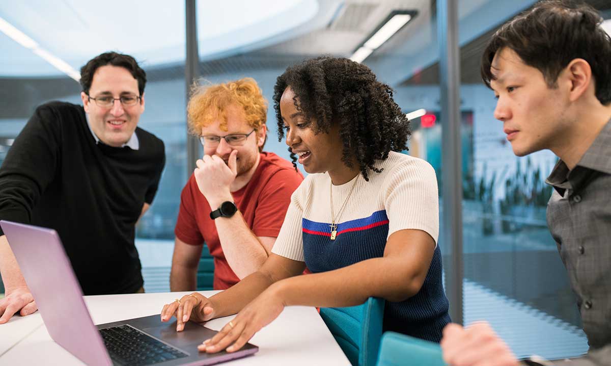 Khoury faculty and students sit and stand around a table viewing research data on a laptop