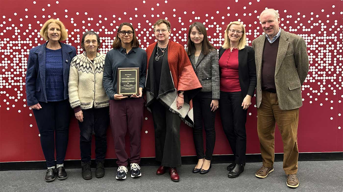 Kylie Bemis stands holding her award, surrounded by Khoury faculty and students