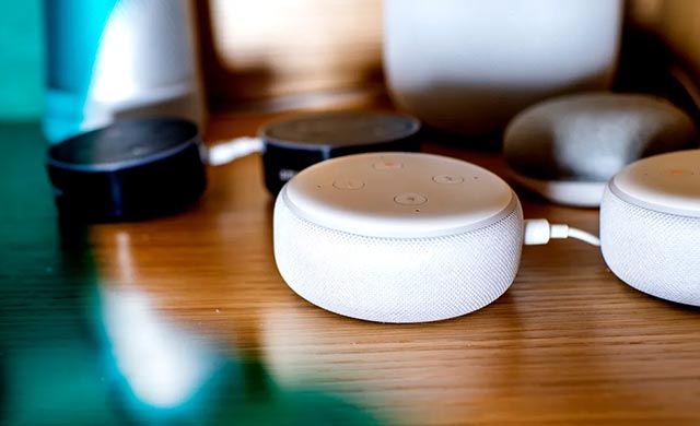 Two white Alexa speakers and two black Alexa speakers sit on a table