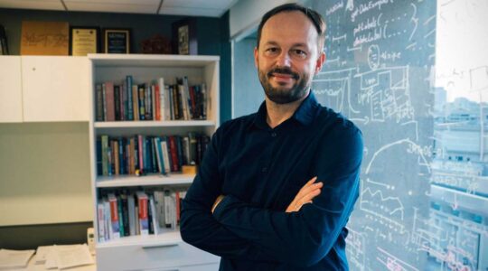 Maciej Kos stands in an office with math equations written on the glass window