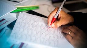 a person writes on a piece of paper using a red pen