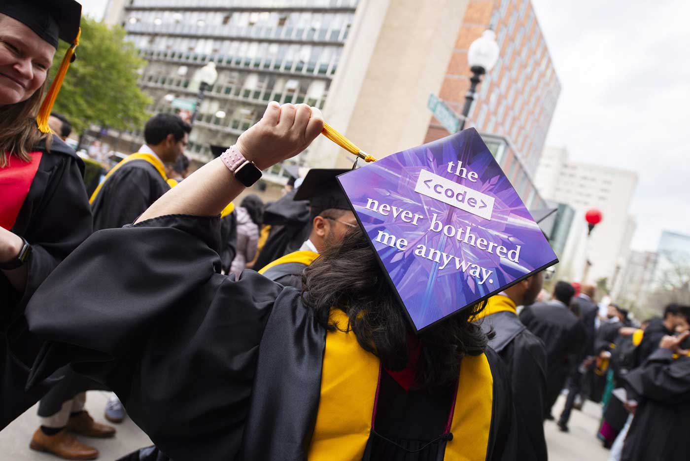 A graduate shows the back of a graduation cap with a sign that says 'the code never bothered me anyway'