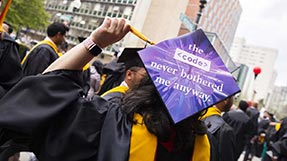 A graduate shows the back of a graduation cap with a sign that says 'the code never bothered me anyway'