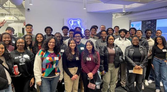 About 35 members of ColorStack pose for a photo in a Northeastern classroom. There is a piece of art with a neon dog head hanging on the wall in the background.