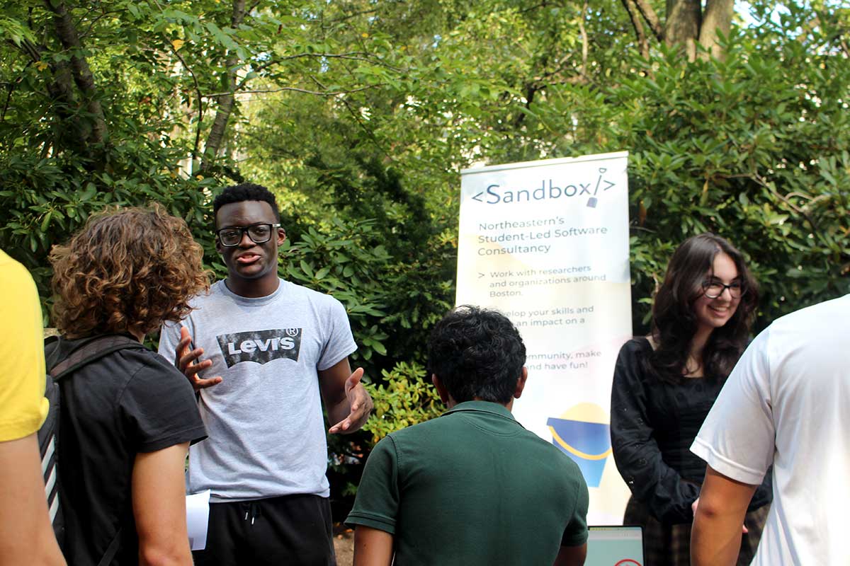 A student member of Sandbox talks about the club to three students.