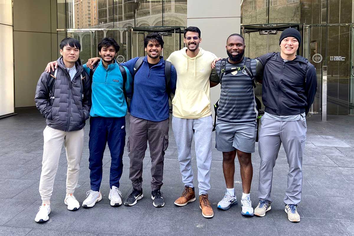 Six members of the Arlington Explorers Society pose with their arms around each others' shoulders on a sidewalk outside a building on the Arlington campus.