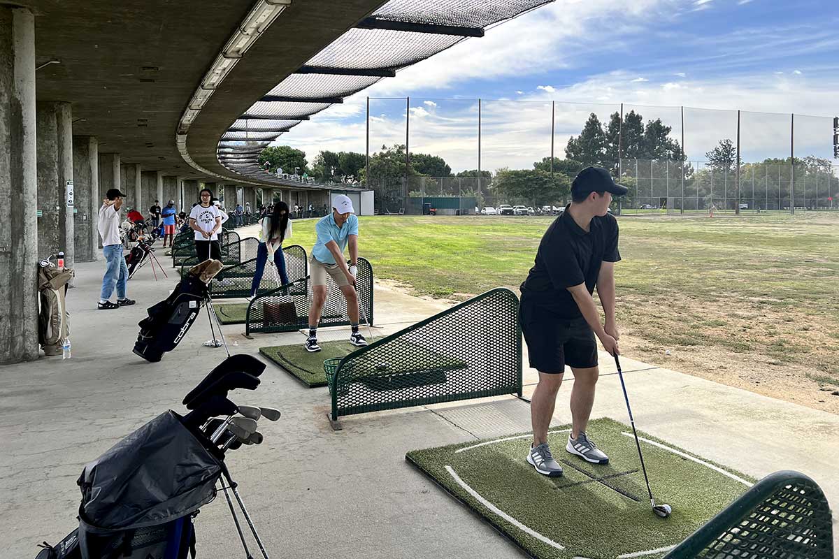 Members of the Bay Area Golf club get ready to hit golf balls at a local driving range. The driving range's net is visible in the background.