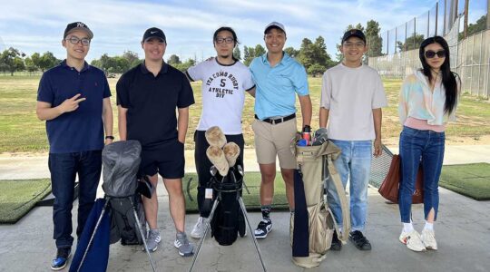 Six members of the Bay Area Golf Club pose for a photo on a sunny day at a local driving range. There are three golf bags standing in front of the club members.