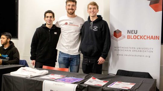 Three members of NEU blockchain pose for a photo as they stand behind the club's table at a Northeastern club fair.