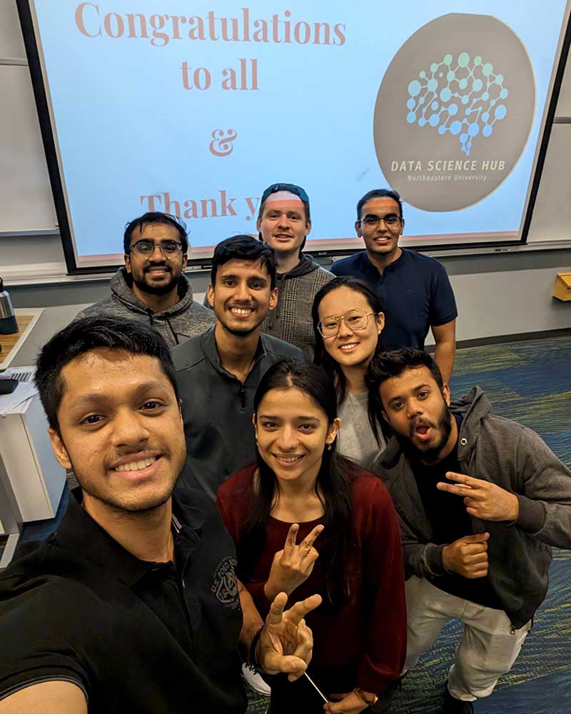 The Data Science Hub pose for a selfie in front of a projection screen in a classroom. There are three students in the front row, two students in the middle row, and three students in the background.