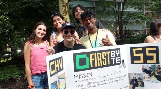 Five members of firstbyte pose for a photo while standing behind their club's poster at a Northeastern club far. The student are smiling and showing peace signs.