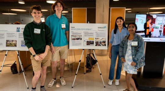 Four members of Oasis stand near their club's poster at a Northeastern club fair in the ISEC building. Two students stand to the left of poster and the other two students stand to the right.