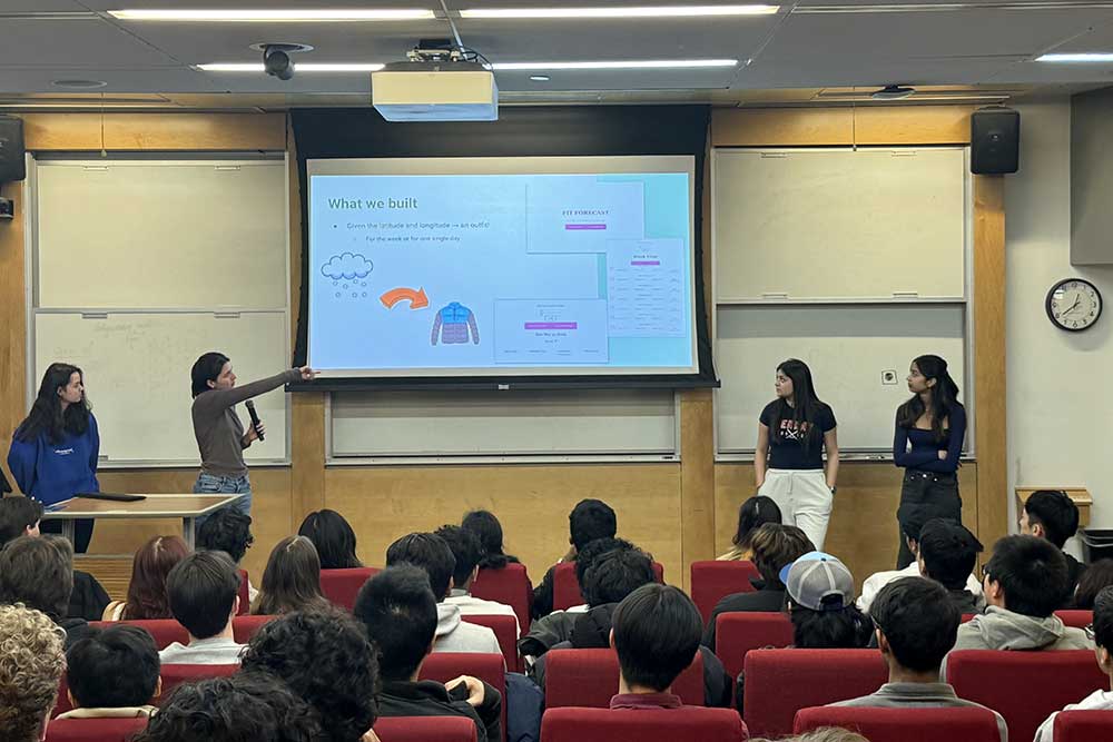 Four members of Oasis stand in front of a projection screen giving a presentation while several other members sit in seat.