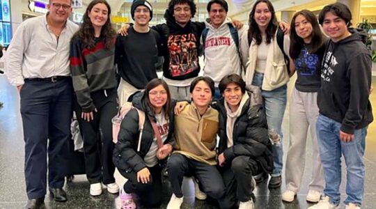 Eleven members of the Society for Hispanic Professional Engineers pose for a photo in a conference center. The first row shows three students kneeling and the other eight students are standing in the back row.