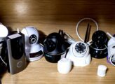 A wooden shelf holds eight networking devices. The networking devices have antennas. Three of the devices are black and the others are white.