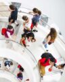 A photo taken from an overhead view of a white spiral staircase in Northeastern's ISEC building. Two levels of the staircase are visible and several students are walking both up and downstairs.