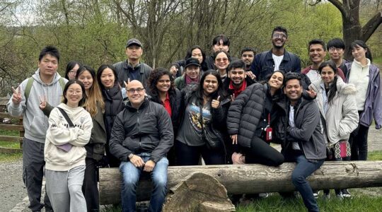 22 members of Khoury College Social Club. pose for a photo at a trailhead. Three of the members are sitting on a large log while the other members stand behind the log.