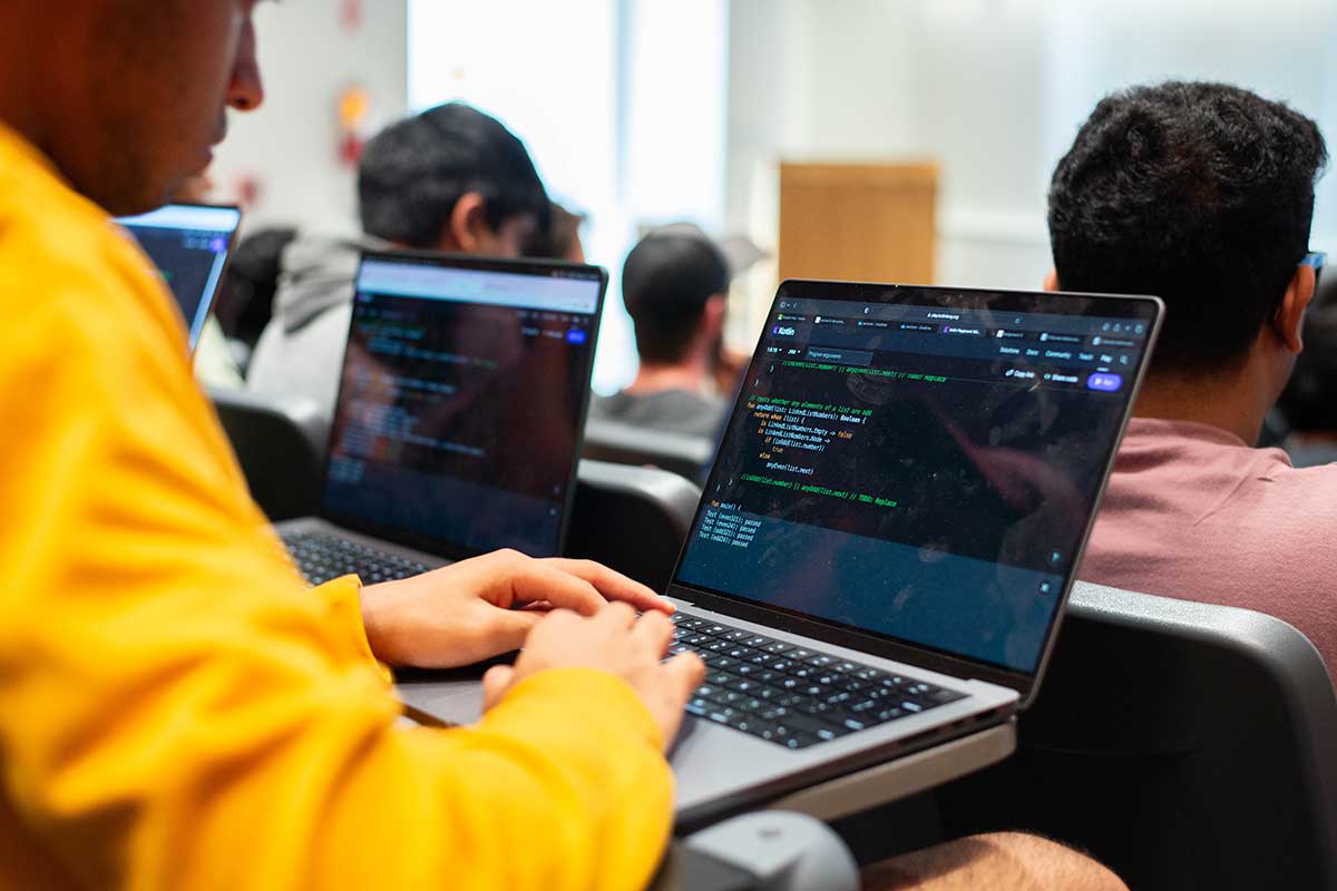 A student types on a laptop while sitting in a Northeastern lecture hall. Other students are sitting in front rows waiting for the class to begin.