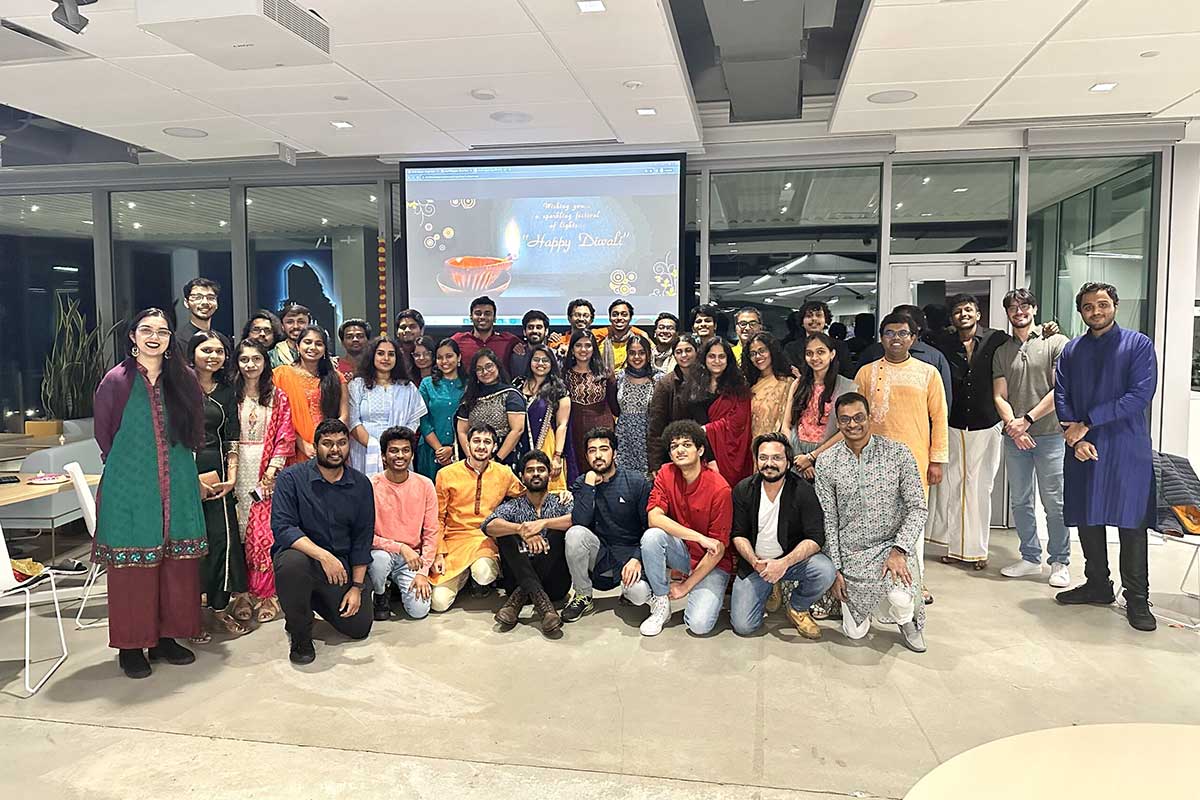 41 members of Namaster pose for a photo at the club's Diwali celebration. In the background, a projection screen shows a message that says, "Happy Diwali".