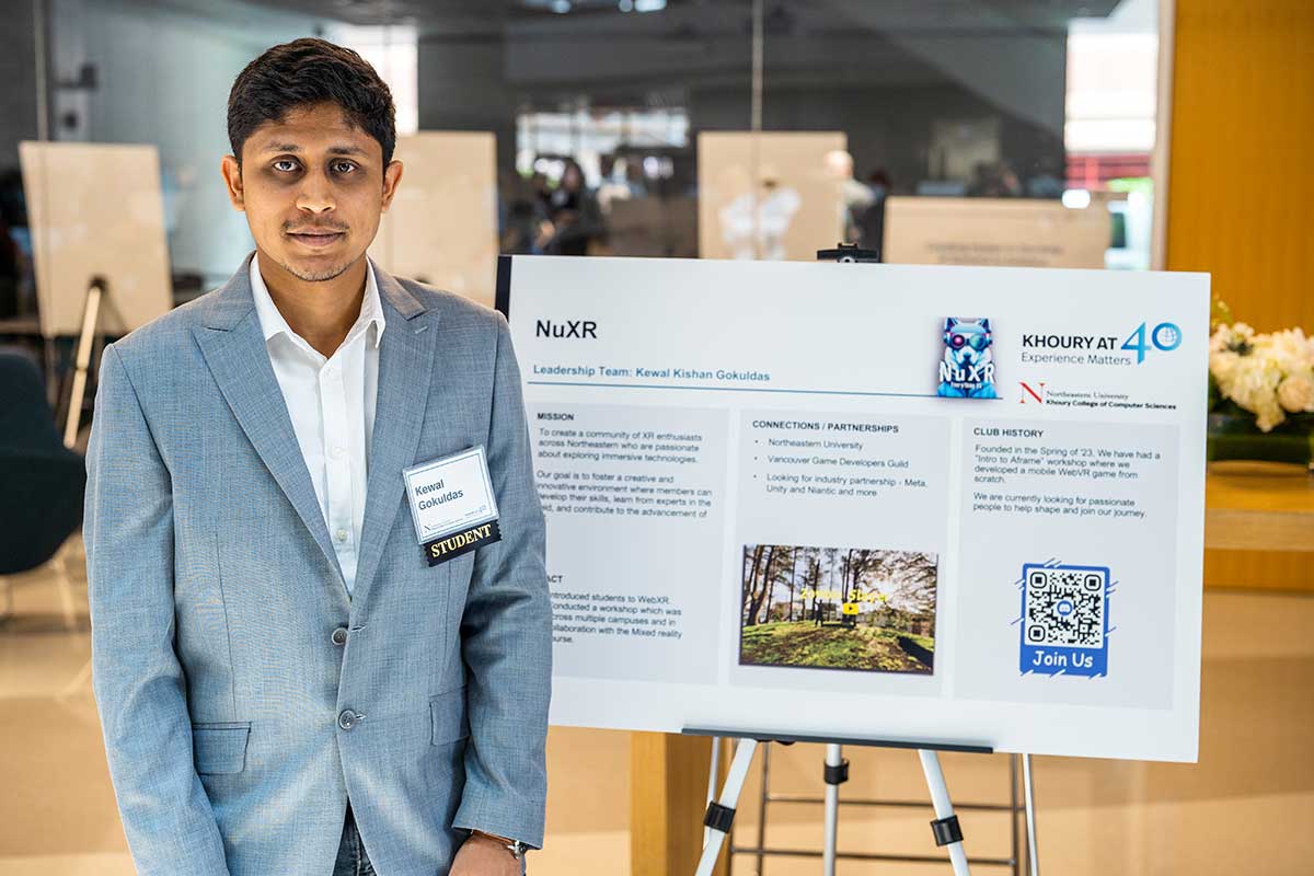 A member of NuXR stands to the left of his club's poster during a club fair. The poster shows the club's mission, partnerships, and history.