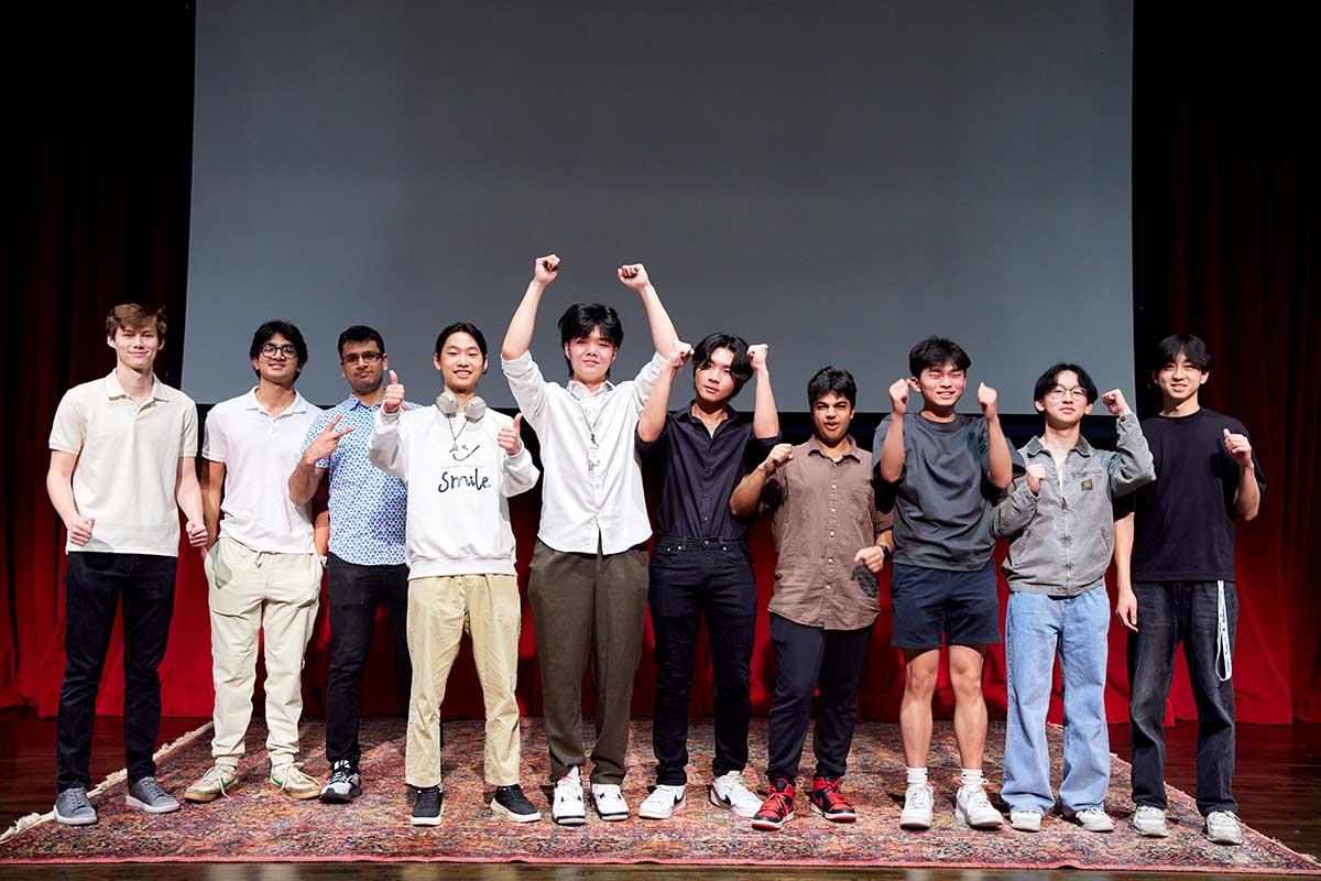 Ten members of Pawhacks pose for a photo on a stage. Several of them are pumping their fists or giving thumbs up signals.