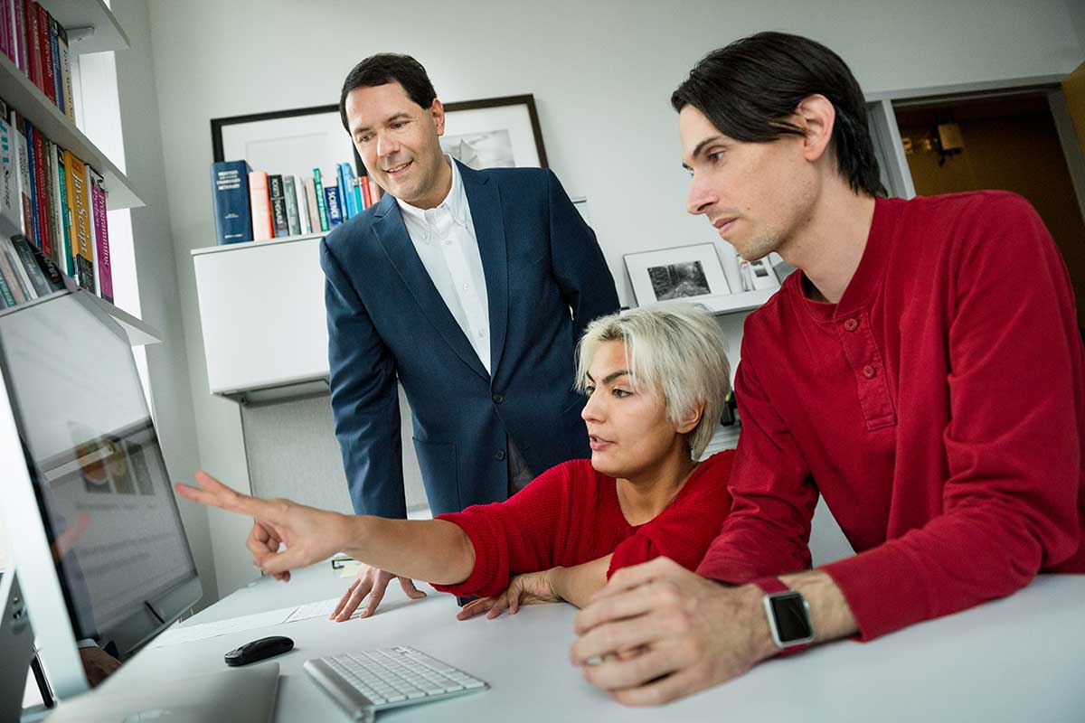 Khoury faculty member Jay Aslam, standing at left, watches while one of his students, sitting in the center, points at a computer monitor. At right, another student views the screen.