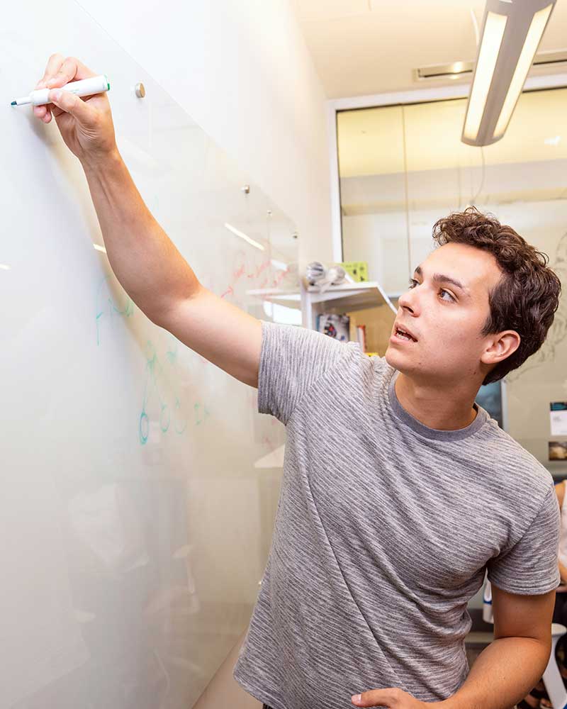 A Khoury student writes on a white board with a green marker. The white board has several green circles drawn on it.