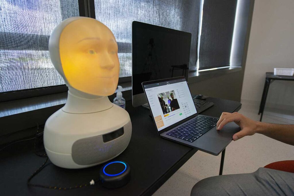 A device shaped like a human head is lit up and connected to a laptop