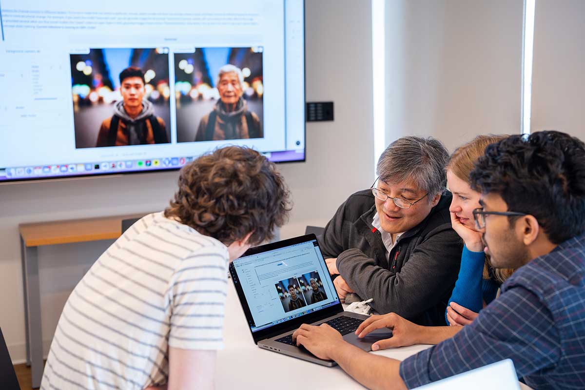 Northeastern faculty member David Bau (third from right) looks at a laptop screen with three researchers huddled around him