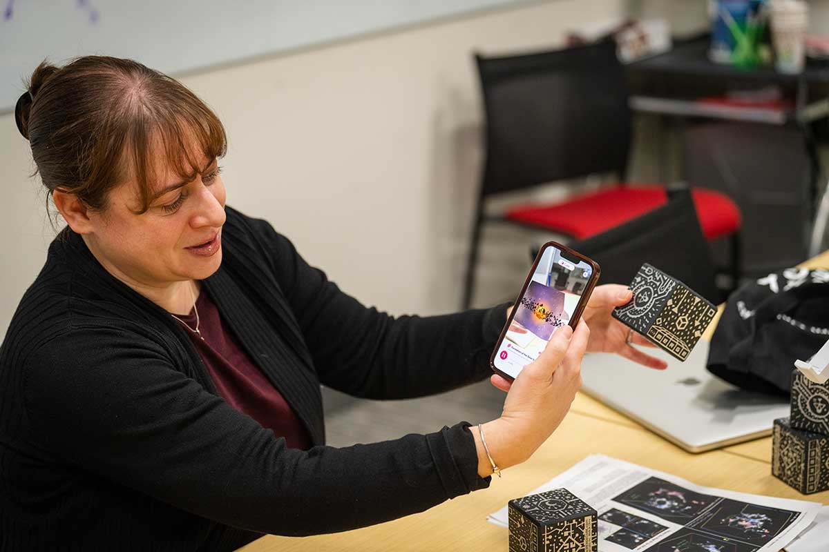 A Khoury faculty members holds a mobile phone in one hand while holding a black piece of paper with a graphic printed in light ink in the other hand.