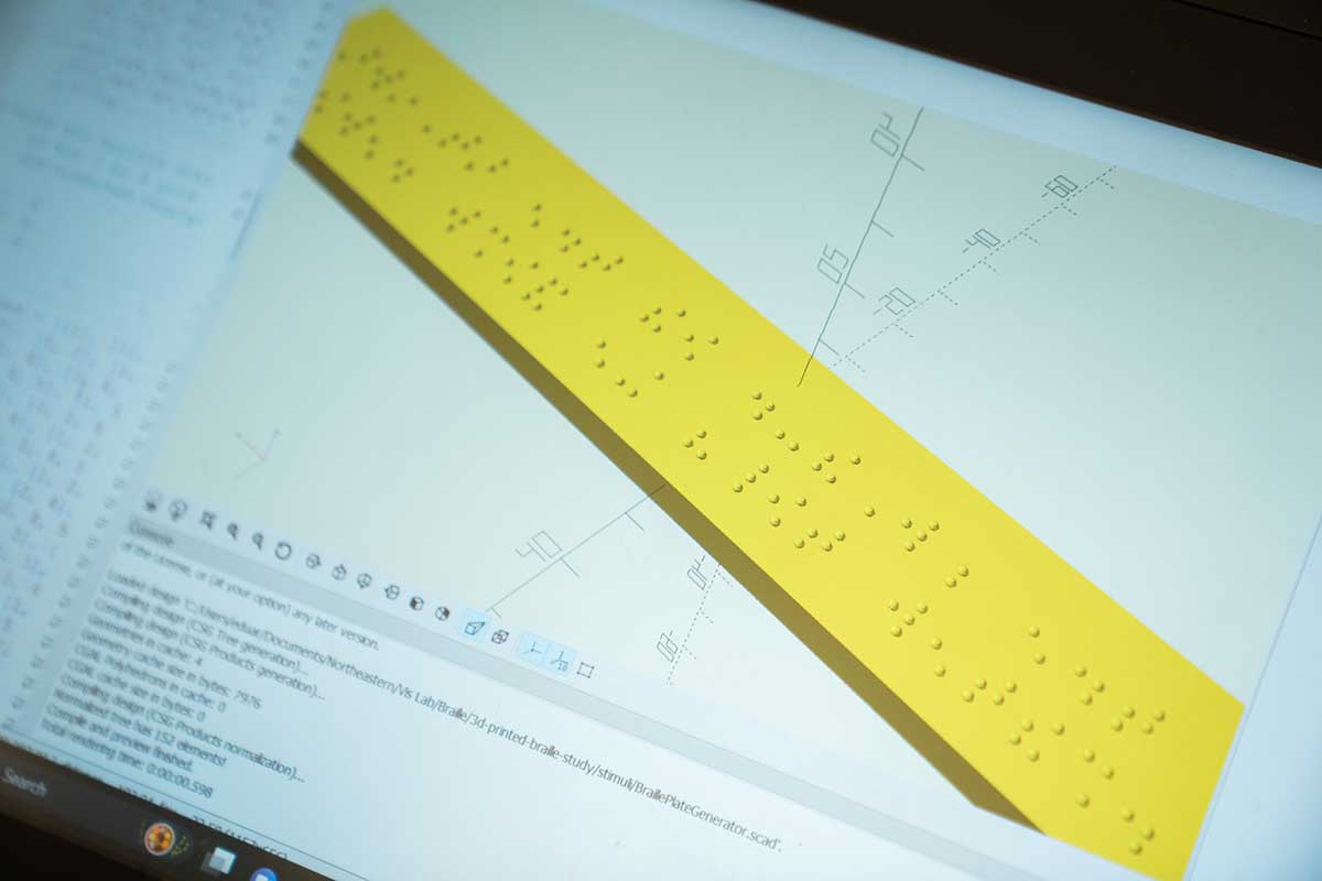 A photo of a computer screen that shows a yellow strip of paper with raised dots on it.