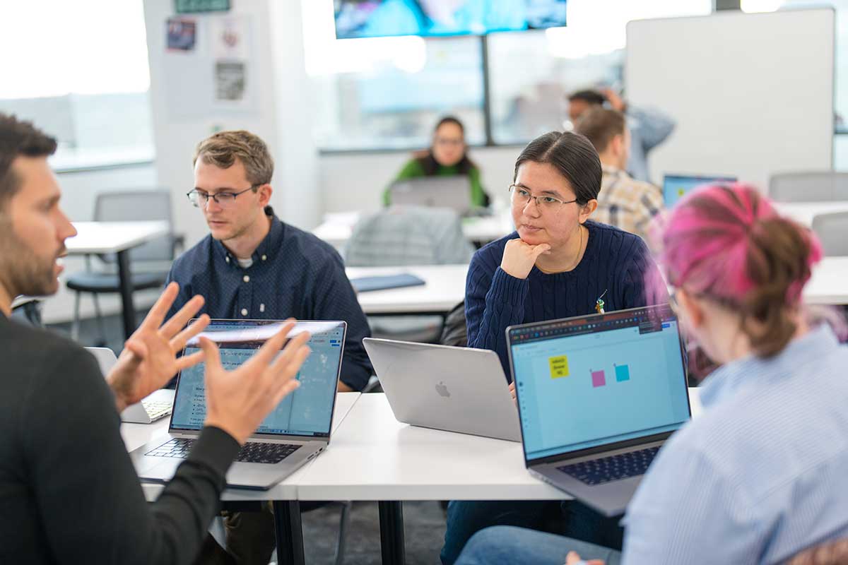 Four students discuss a project while sitting around a large table.