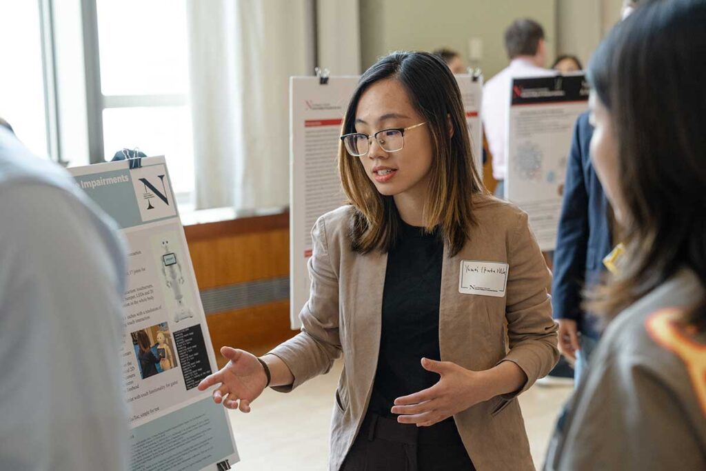 A Khoury student speaks about a research poster at a research exposition to a group of several observers