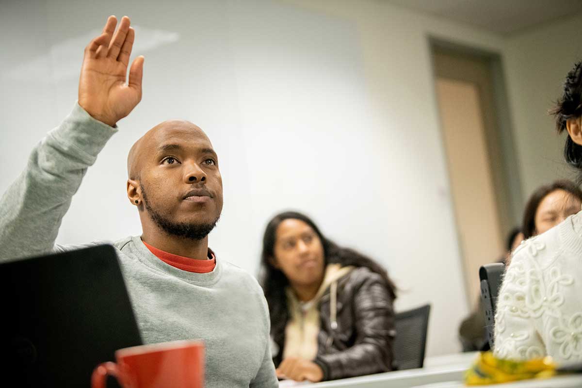 A student sitting at a table raises his hand during a class