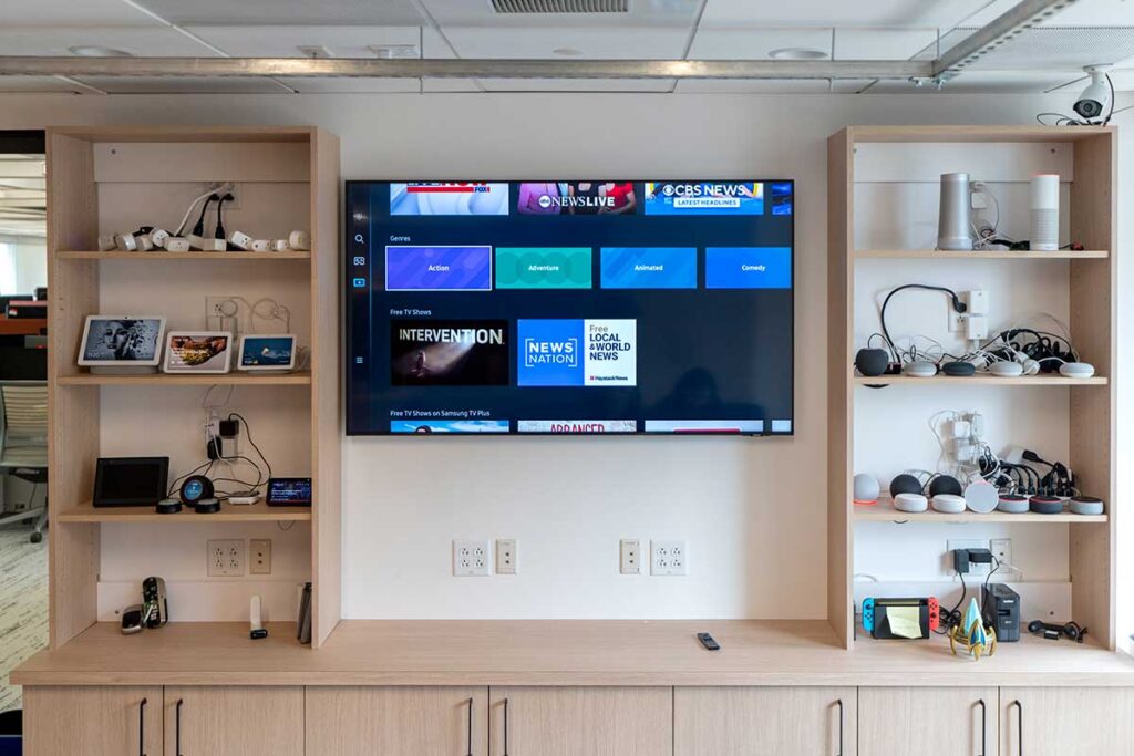 The wall in Northeastern's Wireless Internet of Things Lab. The wall has a flat screen television turned on. There are shelves with wireless devices to the left and right of the television.