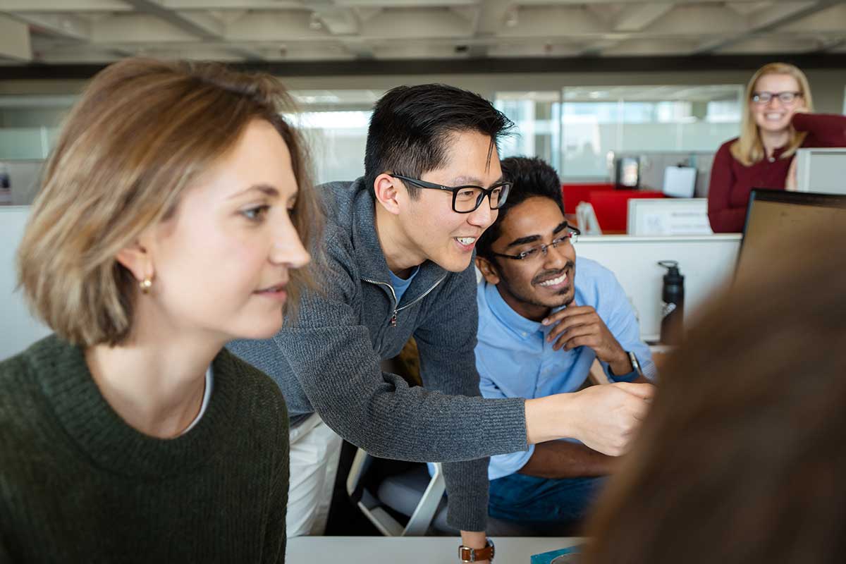 Three students smile while viewing a computer screen in a Khoury lab while a faculty member Olga Vitek looks on in the background.