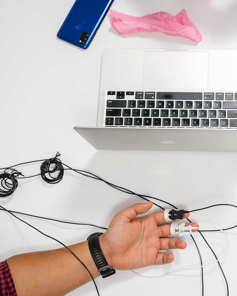 A photo taken from above showing a person's hand with devices clipped to two fingers next to an open laptop and mobile phone.