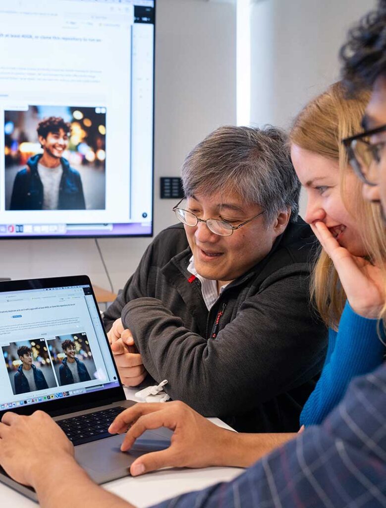 Faculty member DAvid Bau, second from left, views a laptop screen with a group of students. Two students are sitting on Bau's right, and another is setting on Bau's left.