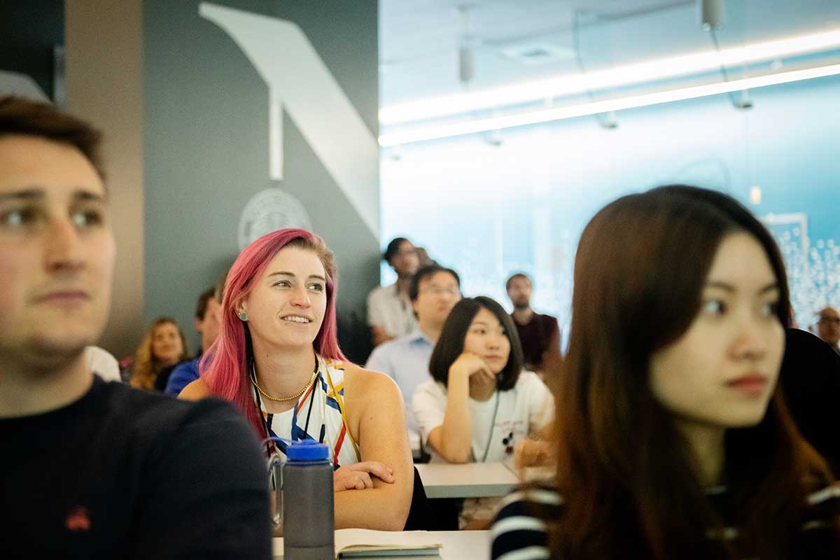 Several students sit at desks viewing a course presentation in a Khoury computer lab. The student in the center of the photo is smiling while watching the presentation.