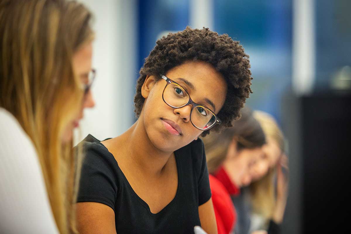 A student looks intently at a student sitting to her left during a class.